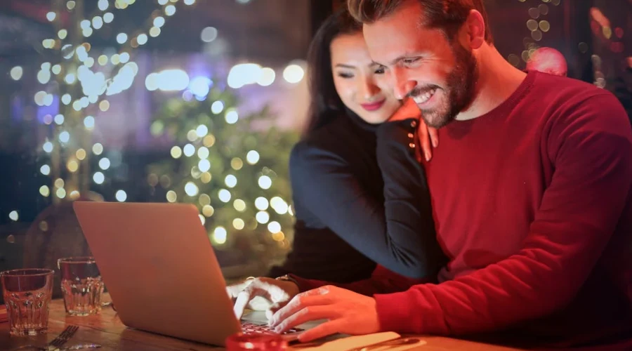 A couple using a laptop at a cozy restaurant with festive bokeh lights, enjoying online shopping together